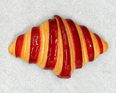 A croissant laminated in red and golden stripes, on baking parchment.